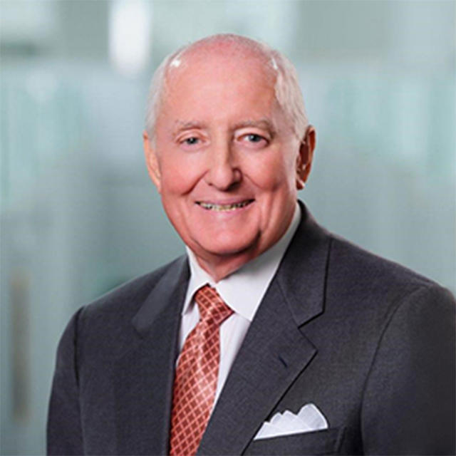 A portrait of a white haired, fair skin man (Mr. Ingram) smiling at the camera in front of a blurred blue background.